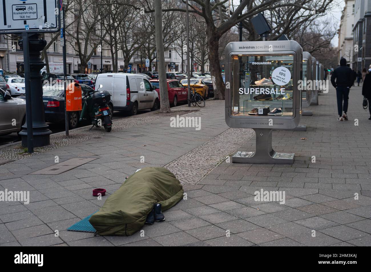 05.02.2022, Berlino, Germania, Europa - la persona senza tetto dorme nel sacco a pelo sul marciapiede di fronte ad un negozio di moda lungo Kurfuerstendamm. Foto Stock