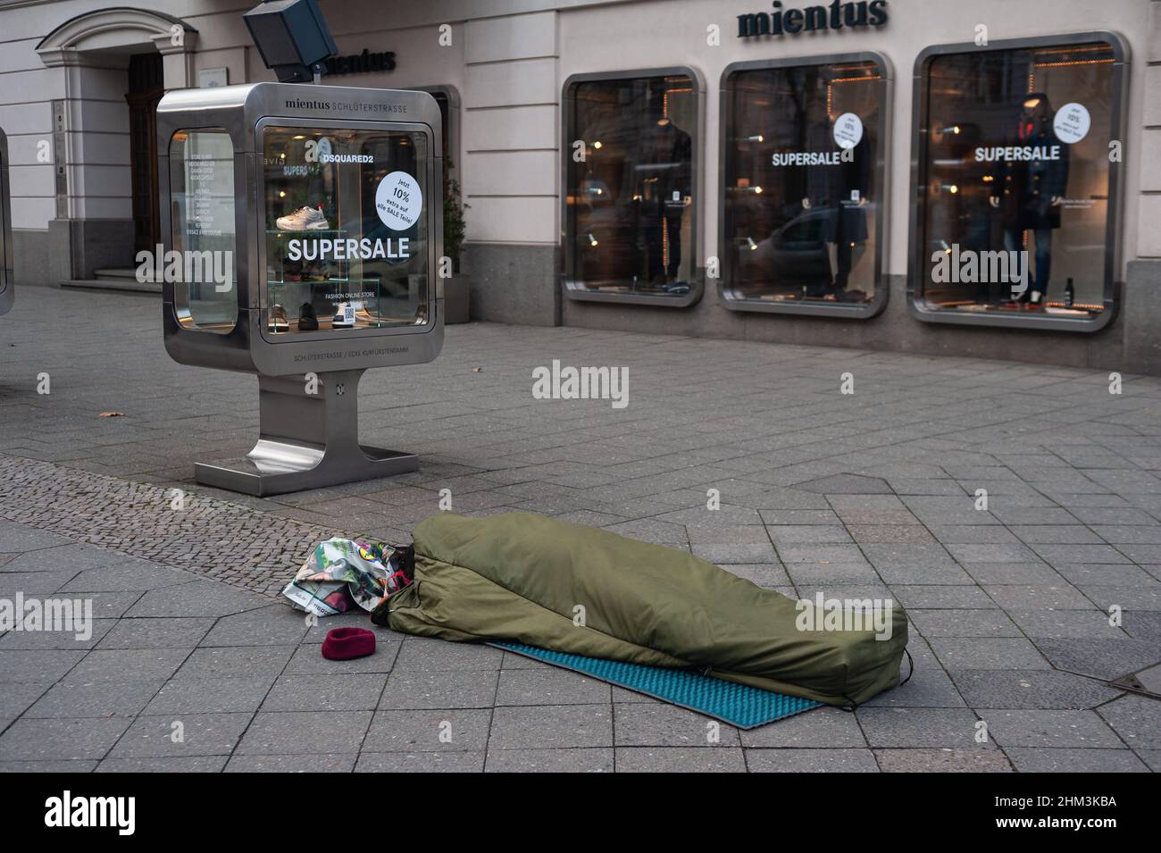 05.02.2022, Berlino, Germania, Europa - la persona senza tetto dorme nel sacco a pelo sul marciapiede di fronte ad un negozio di moda lungo Kurfuerstendamm. Foto Stock