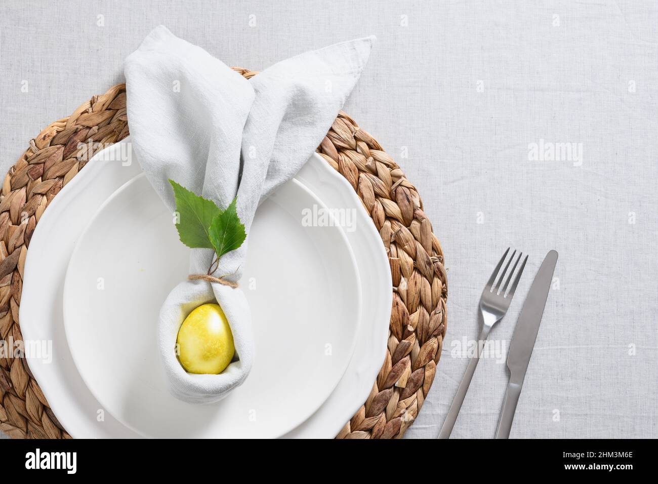 Tavolo pasquale con pulcino giallo, uova, fiori freschi su tovaglia di lino grigio. Cena di eleganza a casa. Vista dall'alto. Religione cristiana tra Foto Stock