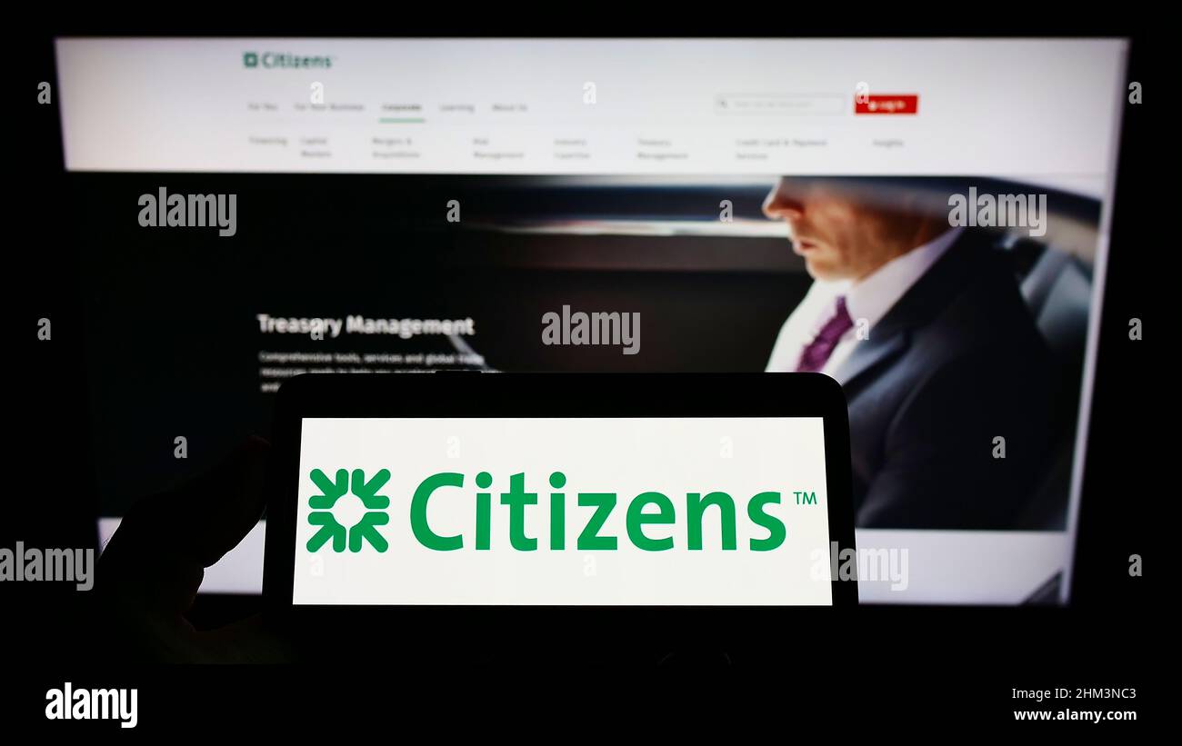 Persona che detiene il cellulare con il logo della società bancaria americana Citizens Financial Group Inc. Sullo schermo di fronte alla pagina web. Mettere a fuoco sul display del telefono. Foto Stock