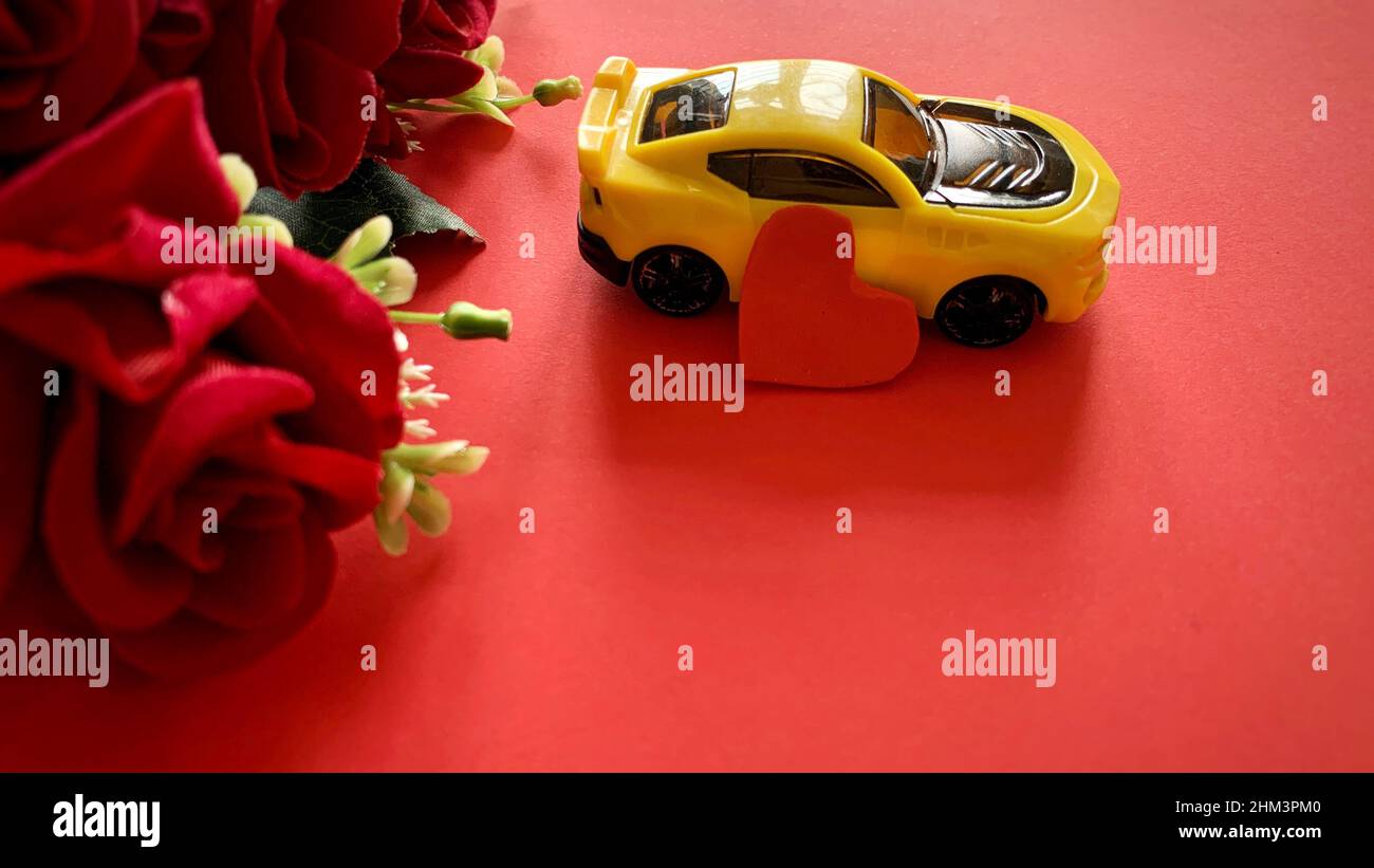 Vista dall'alto delle rose rosse, dell'auto gialla e del cuore con sfondo rosso. Foto Stock