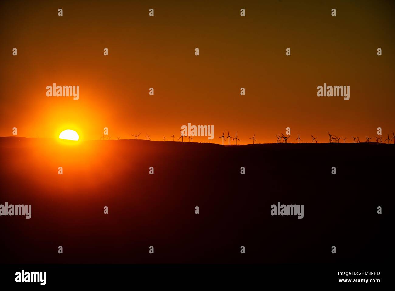 Tramonto su una collina che mette in risalto un windfarm all'orizzonte Foto Stock