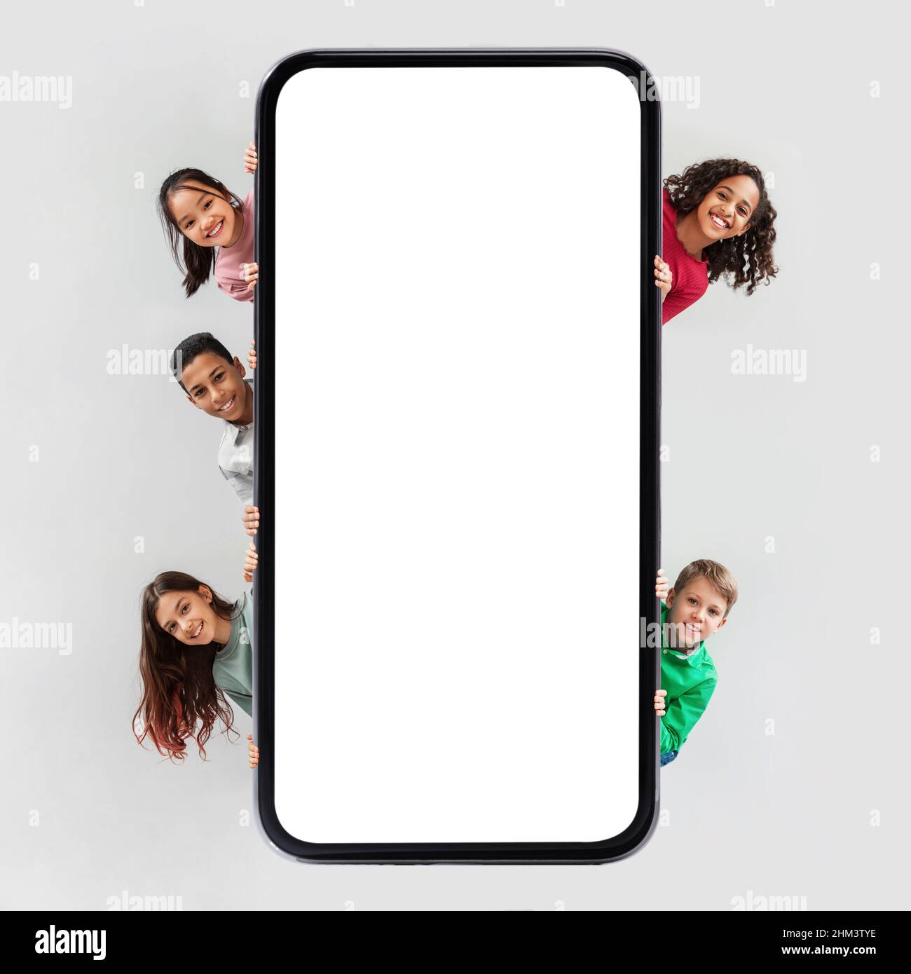 Diversi ragazzi che posano vicino enorme schermo del telefono su sfondo grigio Foto Stock