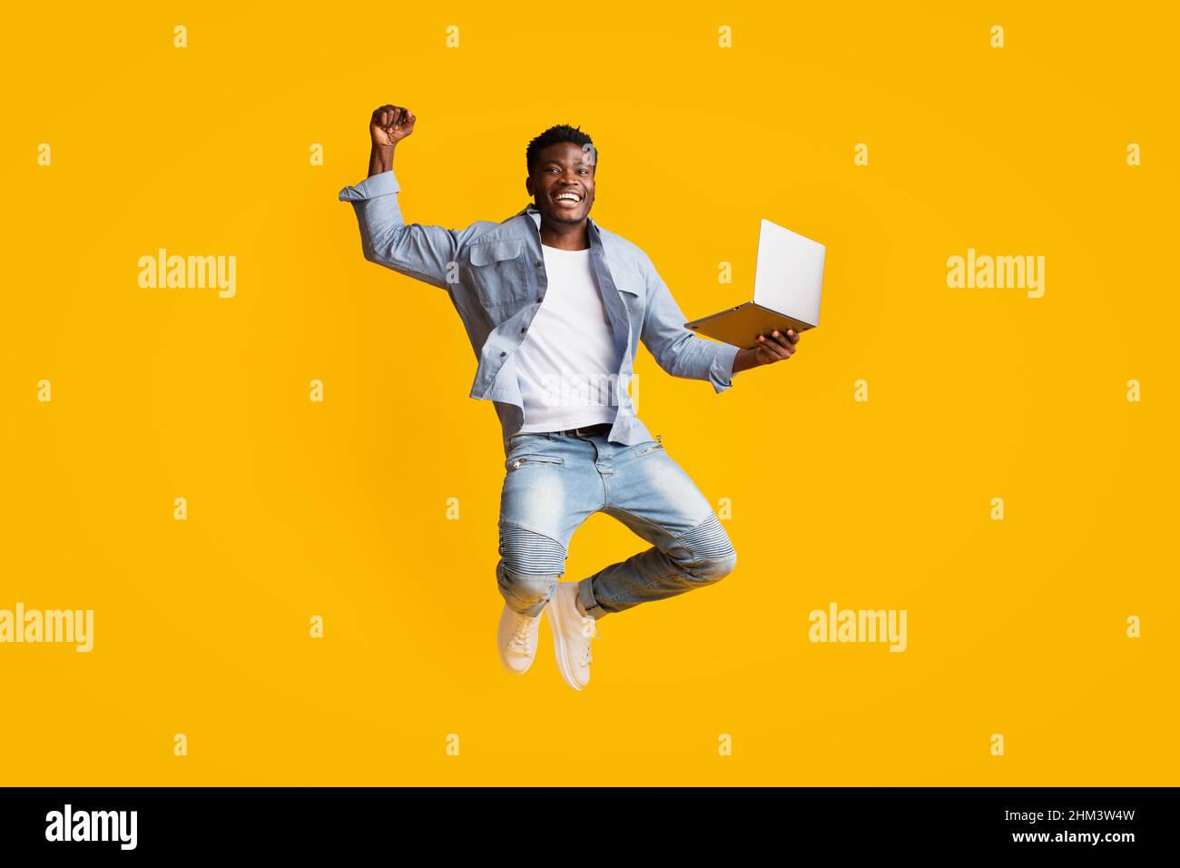 Allegro ragazzo afroamericano che tiene il laptop e salta Foto Stock