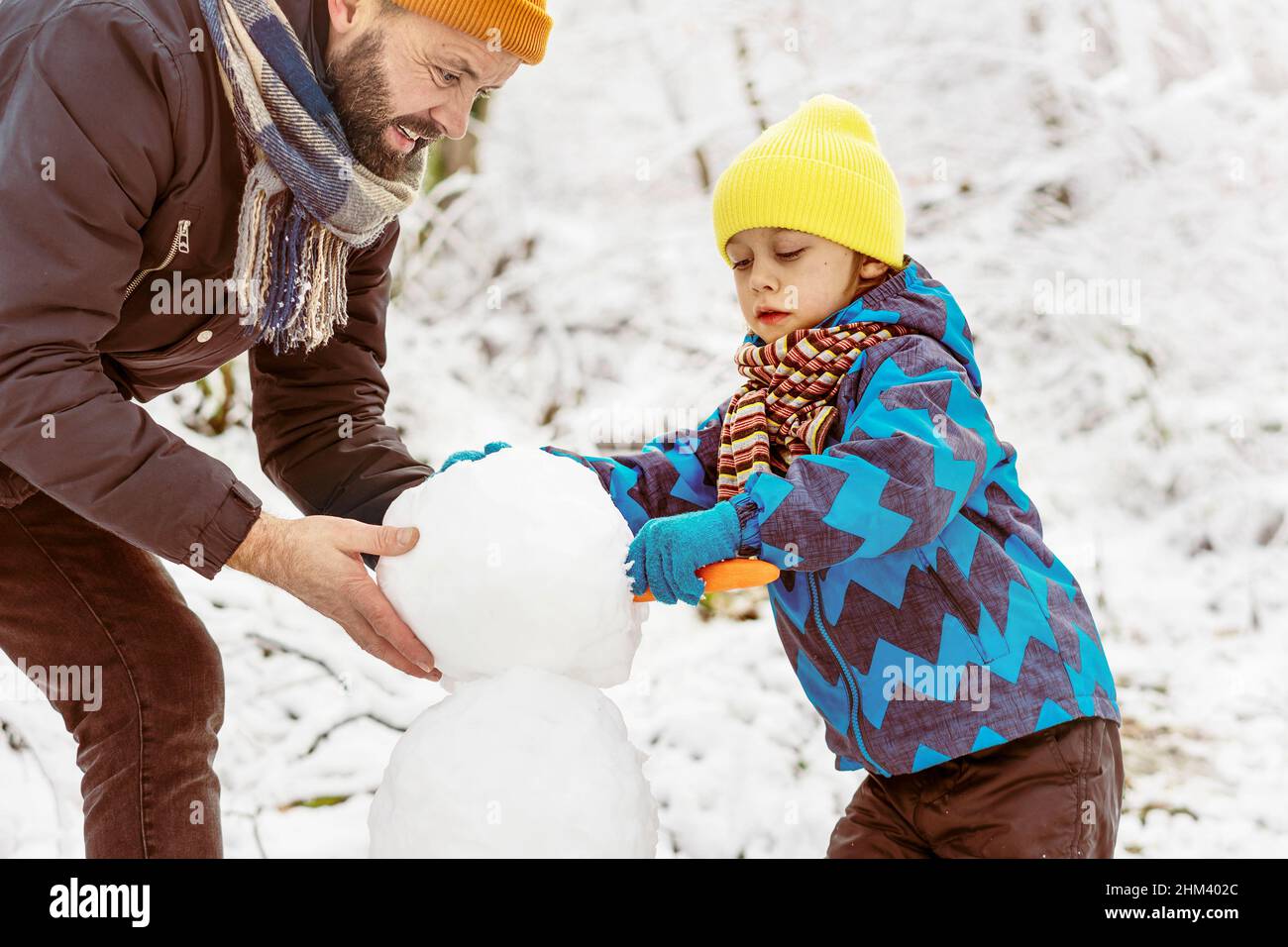 Il ragazzino e il padre si divertono all'aperto sulla neve. Stanno facendo insieme un pupazzo di neve. Foto Stock