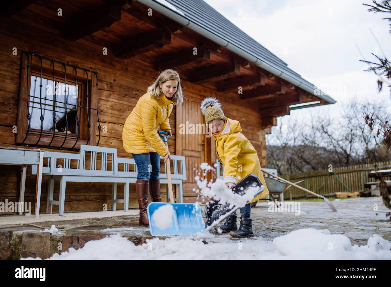 Ragazzo con sindrome di Down con la madre che sgombrava la neve dal sentiero con la pala di fronte a casa. Foto Stock