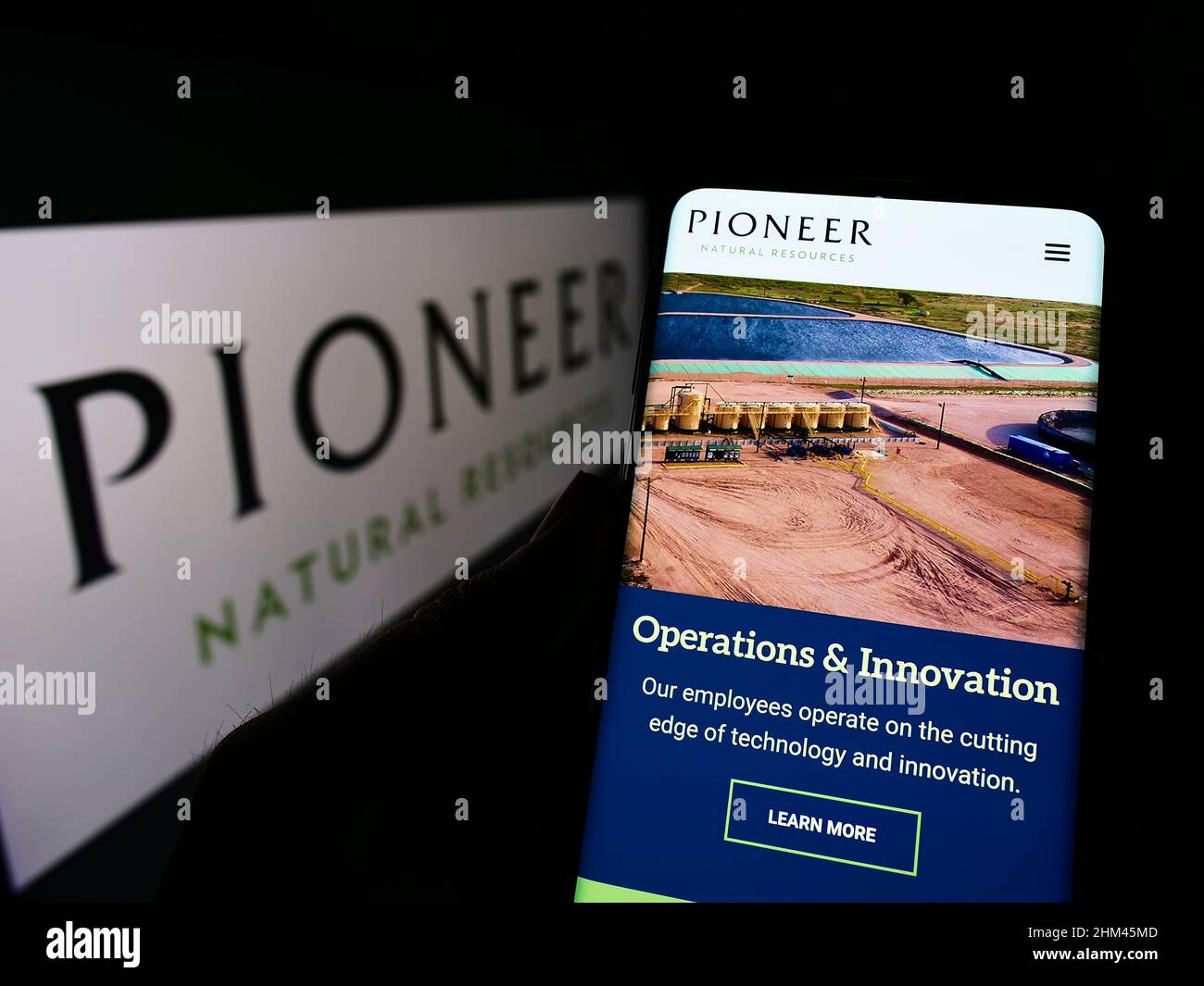Persona che tiene lo smartphone con la pagina web del business statunitense Pioneer Natural Resources Company sullo schermo con il logo. Concentrarsi sul centro del display del telefono. Foto Stock
