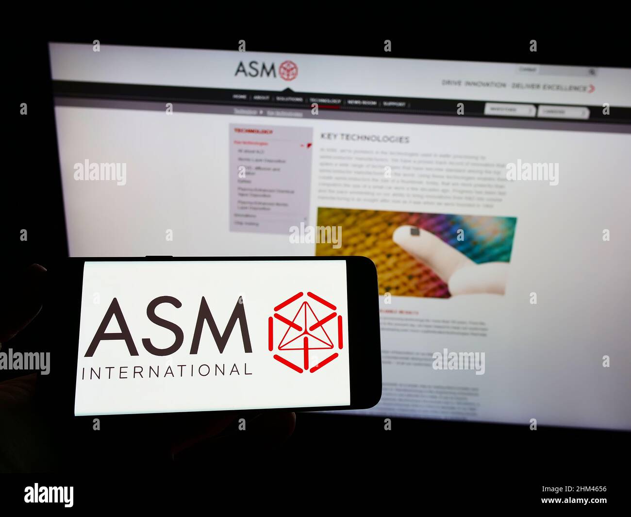 Persona che tiene uno smartphone con il logo della società olandese di semiconduttori ASM International N.V. sullo schermo di fronte al sito web. Mettere a fuoco sul display del telefono. Foto Stock