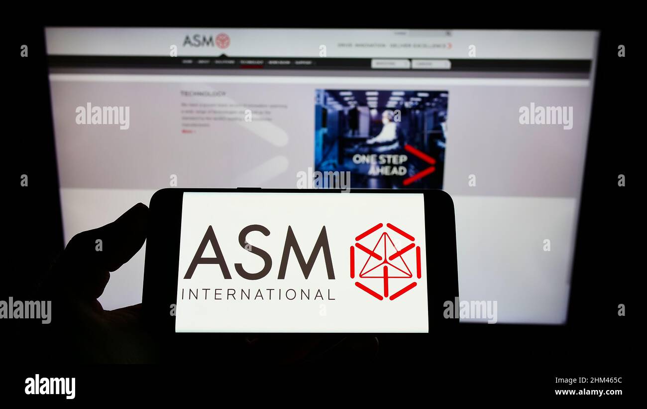 Persona che tiene il telefono cellulare con il logo della società olandese di semiconduttori ASM International NV sullo schermo di fronte alla pagina web. Mettere a fuoco sul display del telefono. Foto Stock