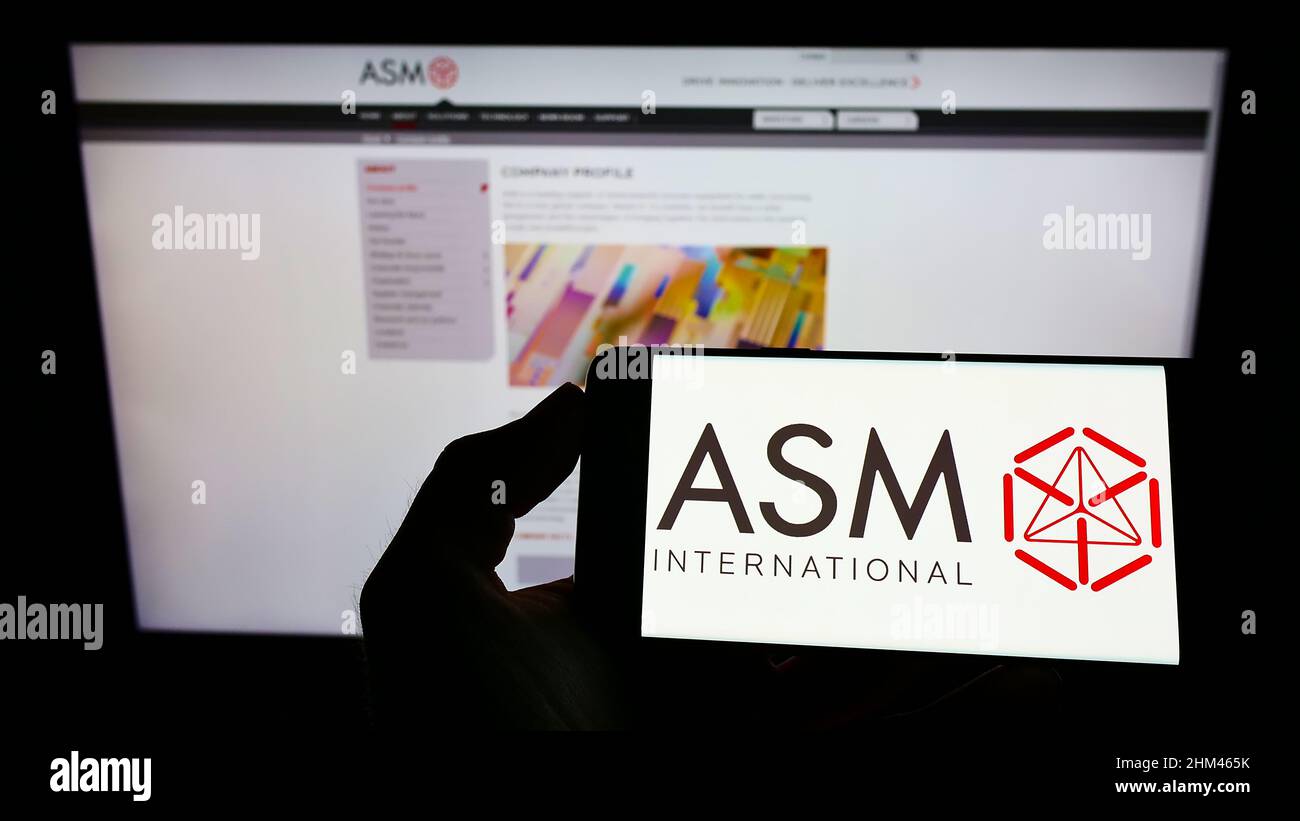 Persona che detiene il cellulare con il logo della società olandese di semiconduttori ASM International N.V. sullo schermo di fronte al sito web. Mettere a fuoco sul display del telefono. Foto Stock