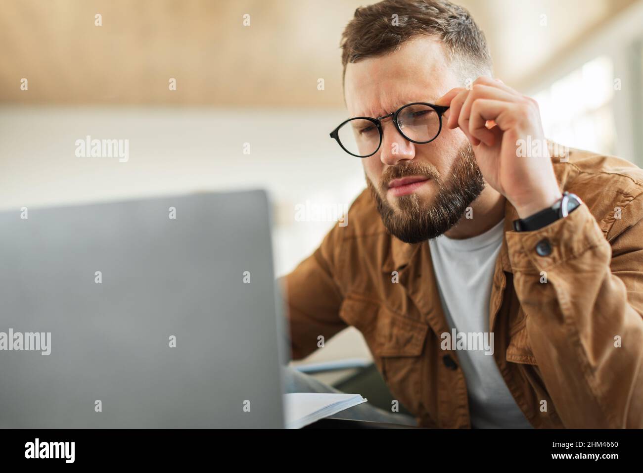 Uomo che guarda il laptop che sbatte gli occhi indossando occhiali da interno Foto Stock