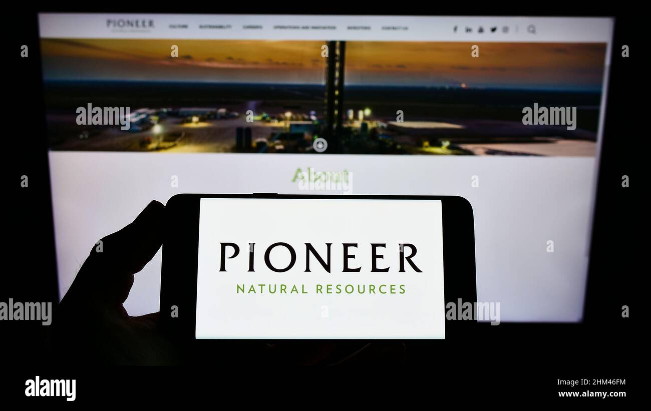 Persona che tiene lo smartphone con il logo della Pioneer Natural Resources Company sul display di fronte al sito web. Mettere a fuoco sul display del telefono. Foto Stock