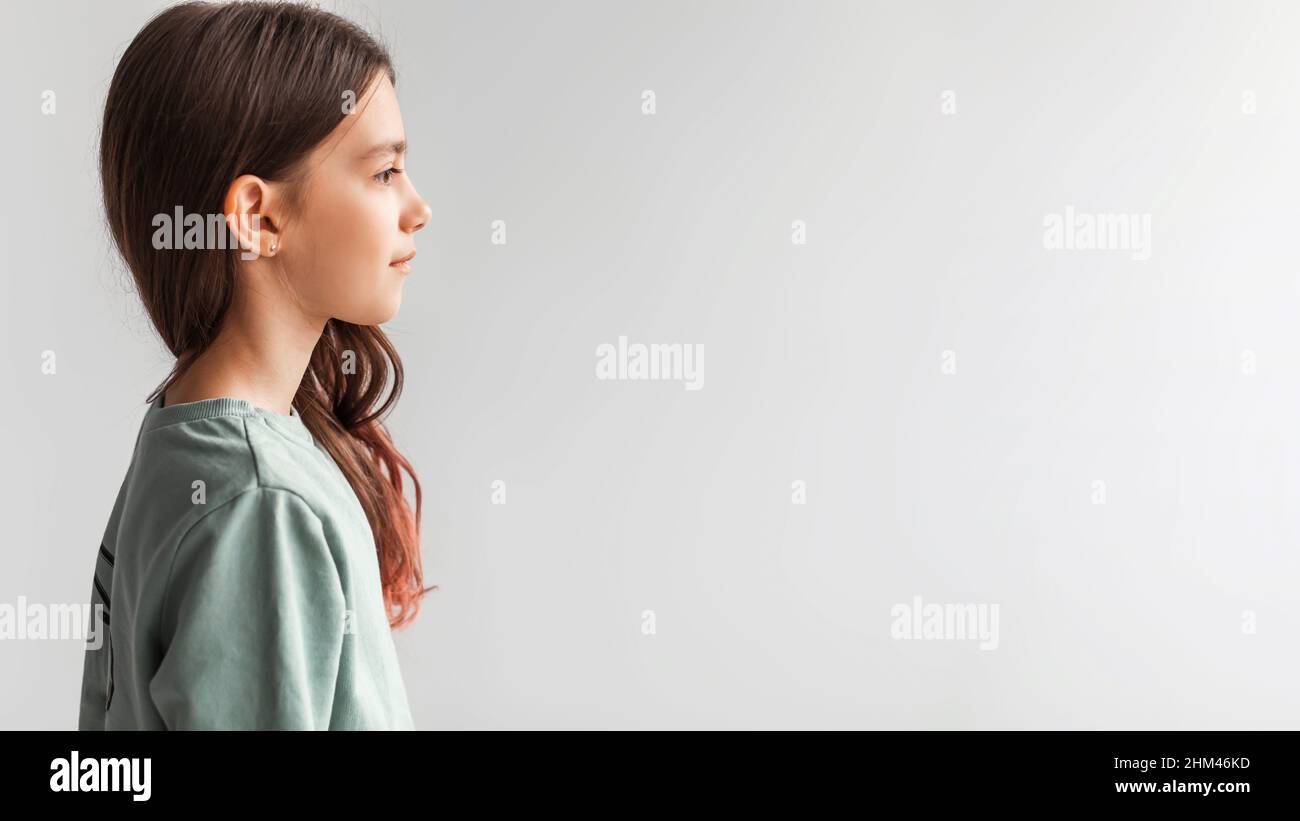 Vista laterale della ragazza seria in piedi guardando da parte, sfondo grigio Foto Stock
