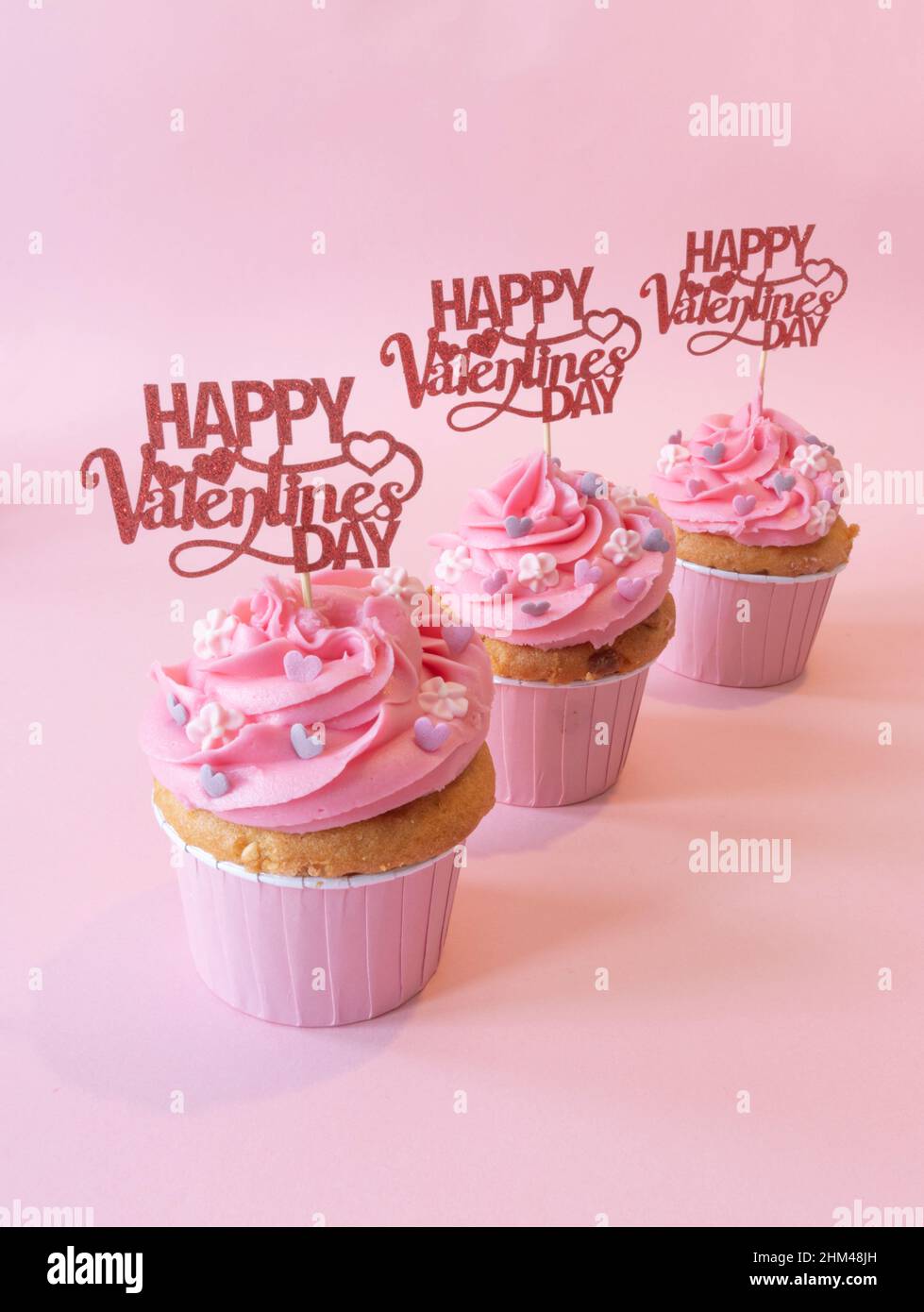 San Valentino Cupcakes con buon San Valentino Sign in ogni torta. La torta è glassata rosa e ha uno sfondo rosa Foto Stock