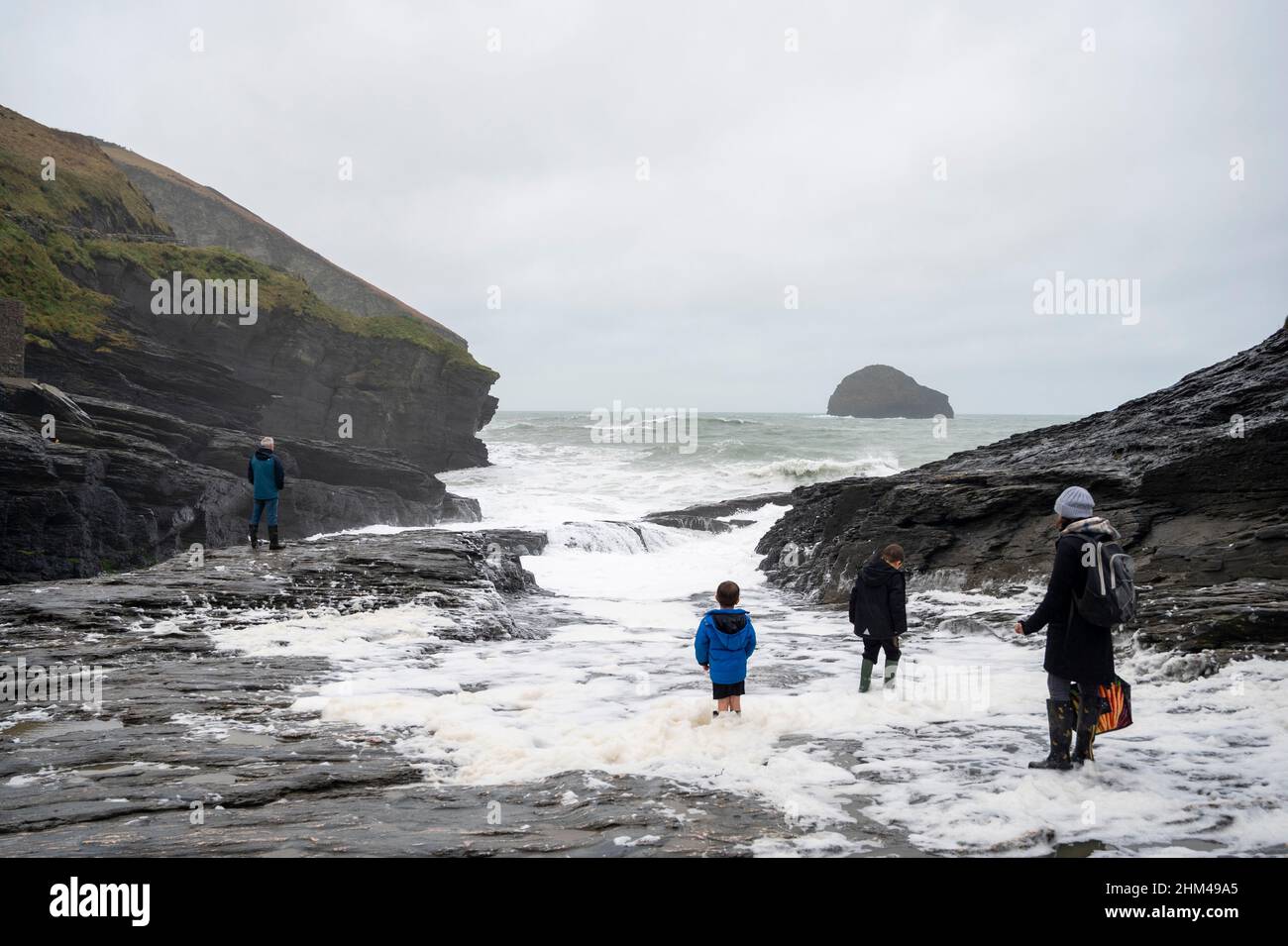 Trebarwith Strand, Cornovaglia, Regno Unito, in inverno con bambini che giocano in schiuma di mare. Foto Stock