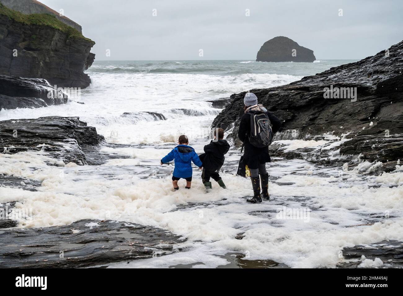 Trebarwith Strand, Cornovaglia, Regno Unito, in inverno con bambini che giocano in schiuma di mare. Foto Stock