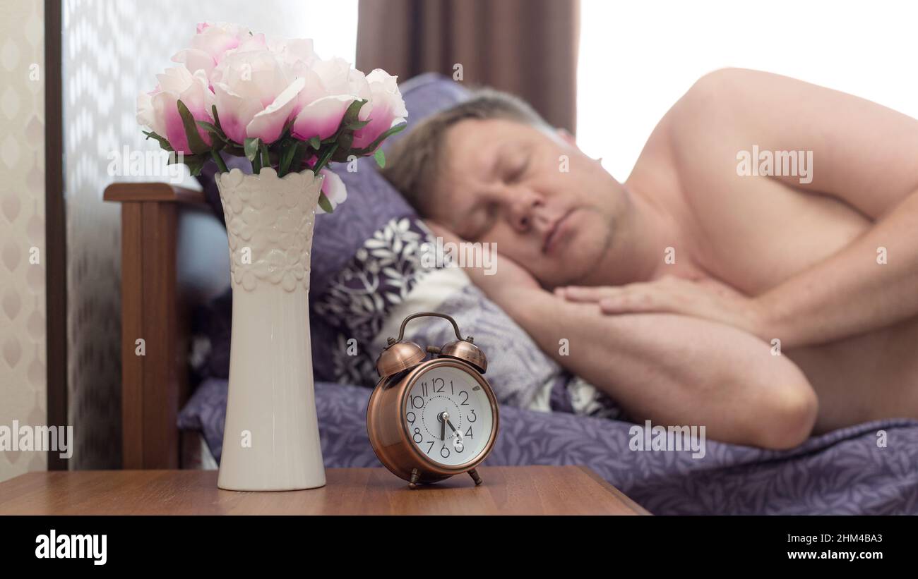 Un uomo adulto di 40-45 anni è addormentato veloce nel suo letto senza sentire la sveglia. Foto Stock