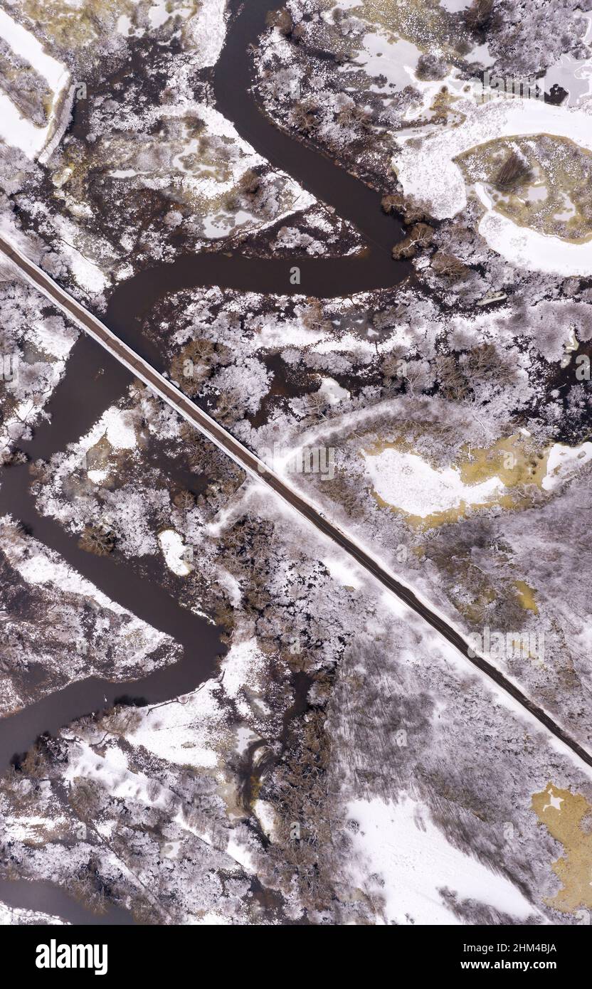 Paesaggio rurale invernale del fiume aereo. Strada con un ponte che attraversa ghiacciata campagna invernale. Foto Stock