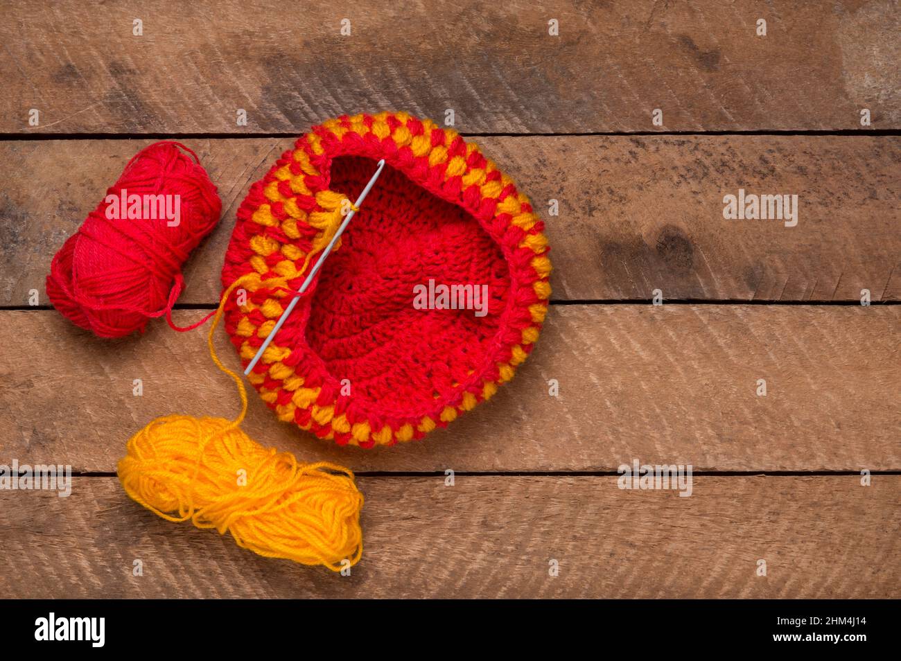 tessuto di lana per maglieria con l'ago, filo tessuto rosso e giallo su un piano di tavolo, concetto di maglieria e lavorazione, spazio copia Foto Stock