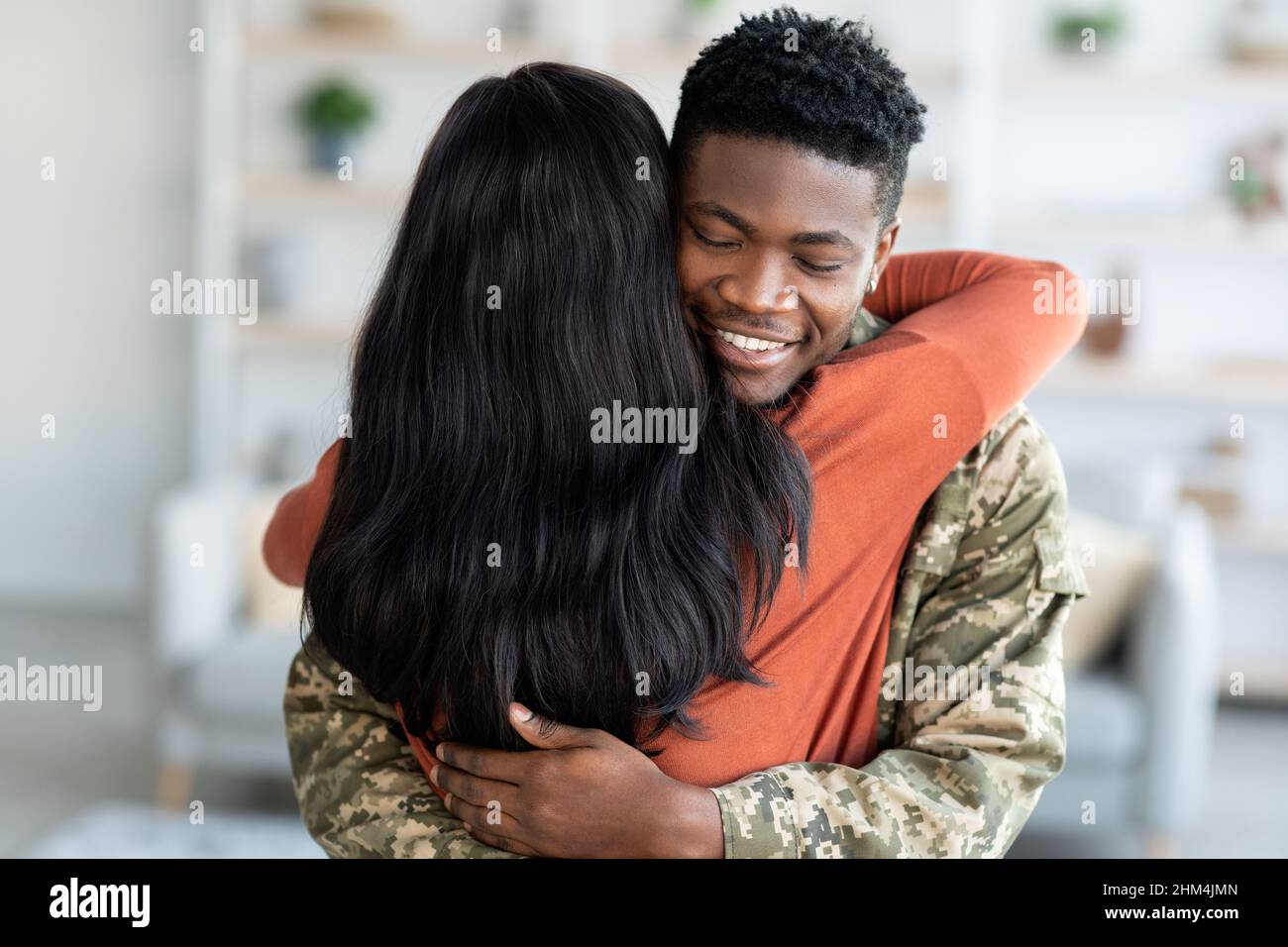 Concetto di ritorno a casa. Happy Black Soldier Man abbraccia la moglie dopo aver tornato a casa Foto Stock
