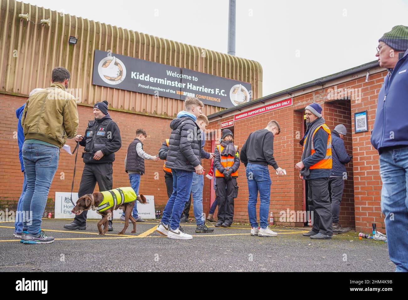 Cane gestore e cane al lavoro che controlla i tifosi in coda ad un ingresso di gioco di calcio britannico. Foto Stock