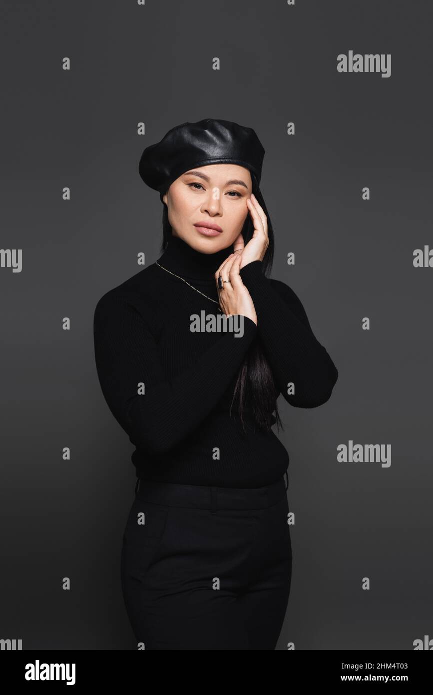 Elegante donna asiatica in beretto e dolcevita volto a contatto isolato su grigio scuro Foto Stock
