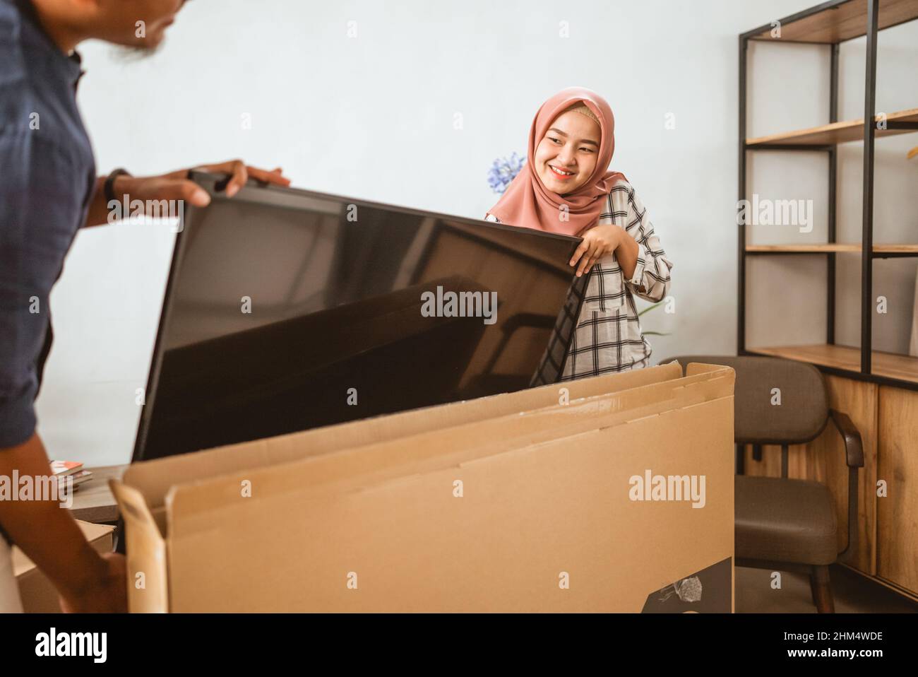 Coppia musulmana che trasporta lo schermo piatto della televisione nella loro casa moderna Foto Stock