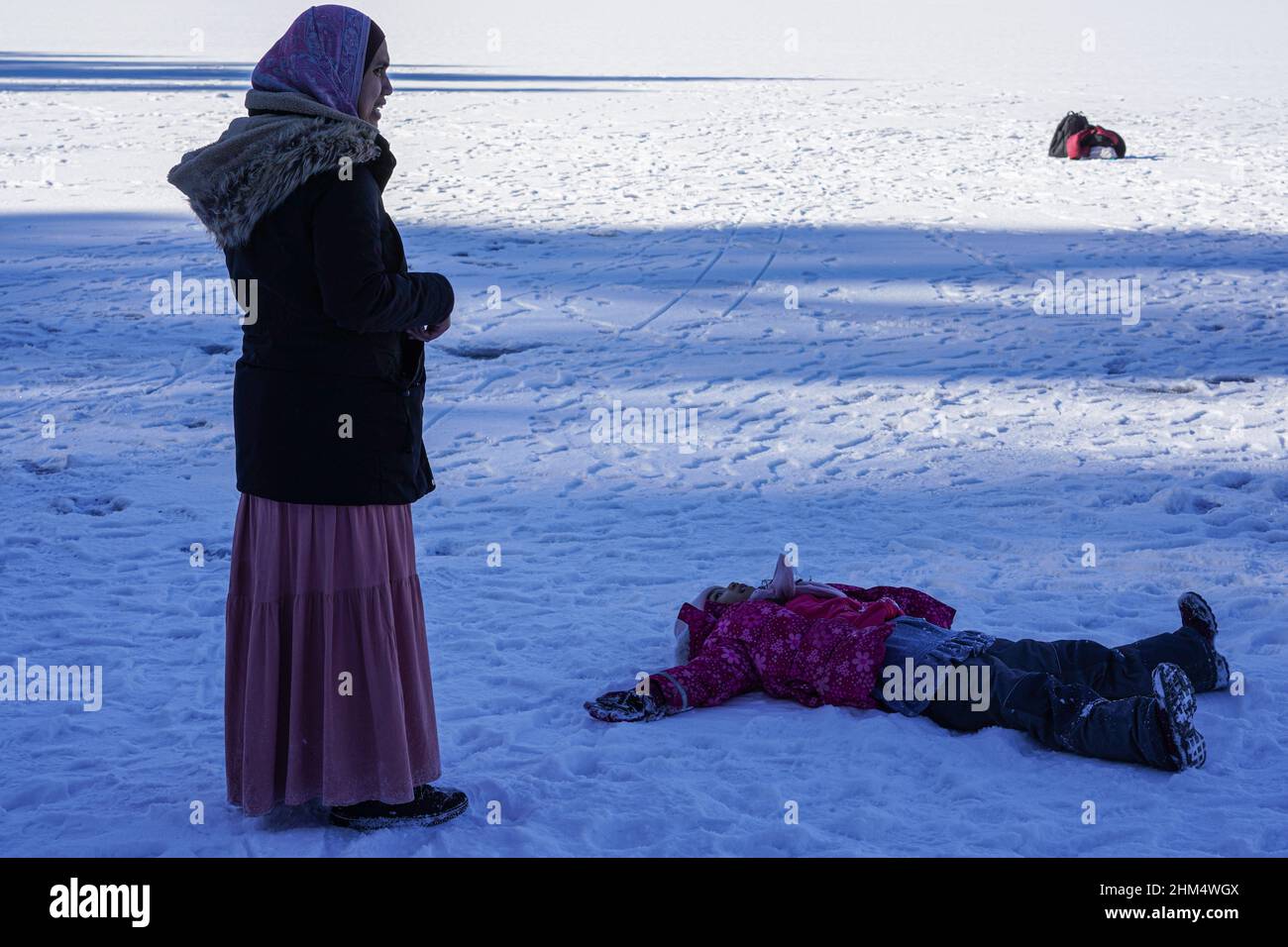 Turista asiatico femminile con foulard è in piedi sulla superficie ghiacciata di Eibsee, Zugspitze.. Il bambino si è posato a terra nella neve. Foto Stock