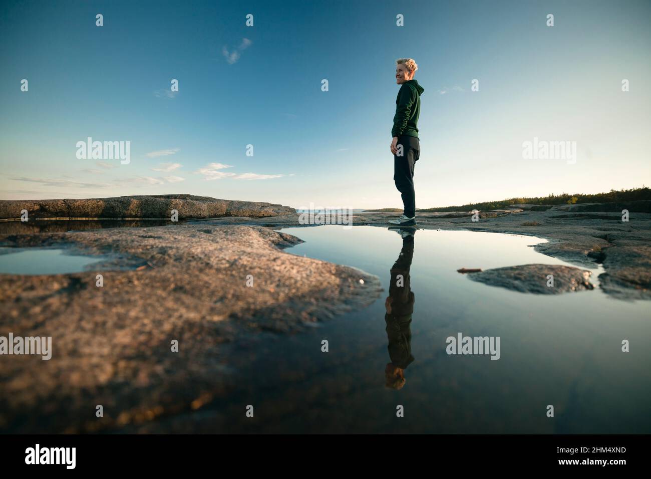 Donna in piedi sulla costa e riflettendo in pozzanghere Foto Stock