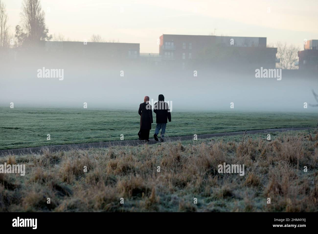 I pedoni camminano in un parco coperto dalla nebbia a Ilford, Londra orientale, al mattino, quando la temperatura è scesa. Foto Stock