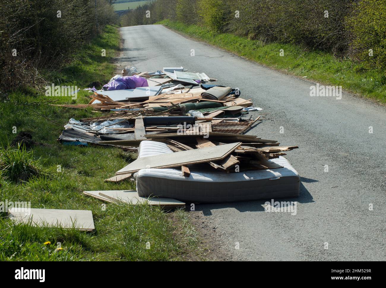 Vista ravvicinata dei rifiuti domestici, tra cui un materasso, scaricati incautamente su una strada di campagna stretta e creando un pericolo per la guida. Foto Stock Vista ravvicinata dei rifiuti domestici, tra cui un materasso, scaricati incautamente su una strada di campagna stretta e creando un pericolo per la guida. Foto Stock