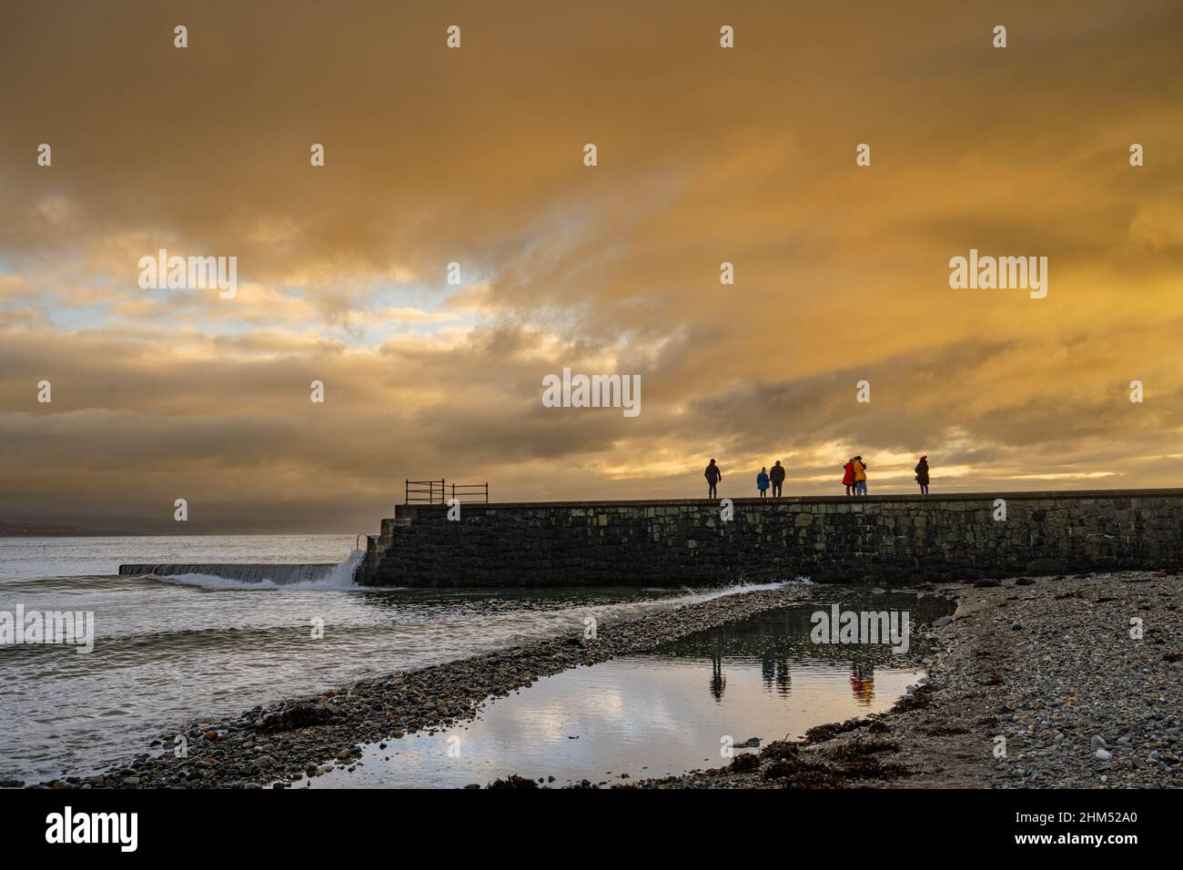 Persone sul frangiflutti al Criccieth North Wales al Tramonto Foto Stock