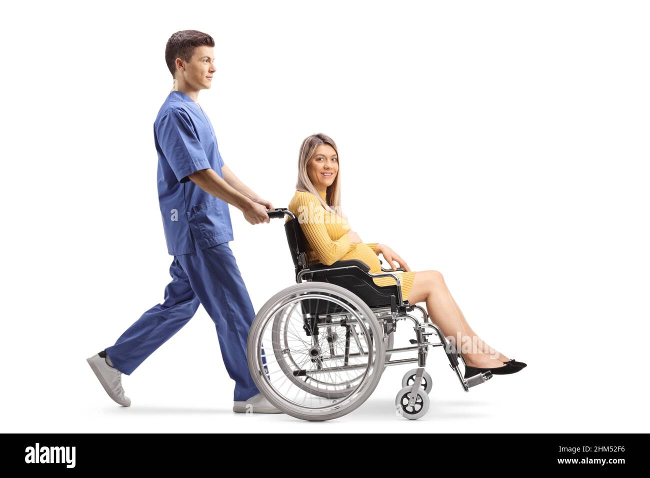 Colpo di profilo a tutta lunghezza di un'infermiera maschio che spinge una donna incinta in una sedia a rotelle isolata su sfondo bianco Foto Stock