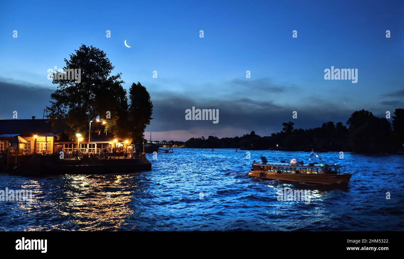 Trasporto pubblico in barca di legno nel pomeriggio nel fiume con le acque blu espressive e mezza luna sullo sfondo a Tigre, Buenos Aires. Foto Stock
