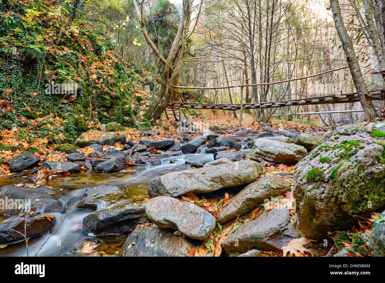 Ponte sospeso da foto a lunga esposizione, foto a ponte ad angolo basso e flusso d'acqua intorno alle pietre. Foto Stock