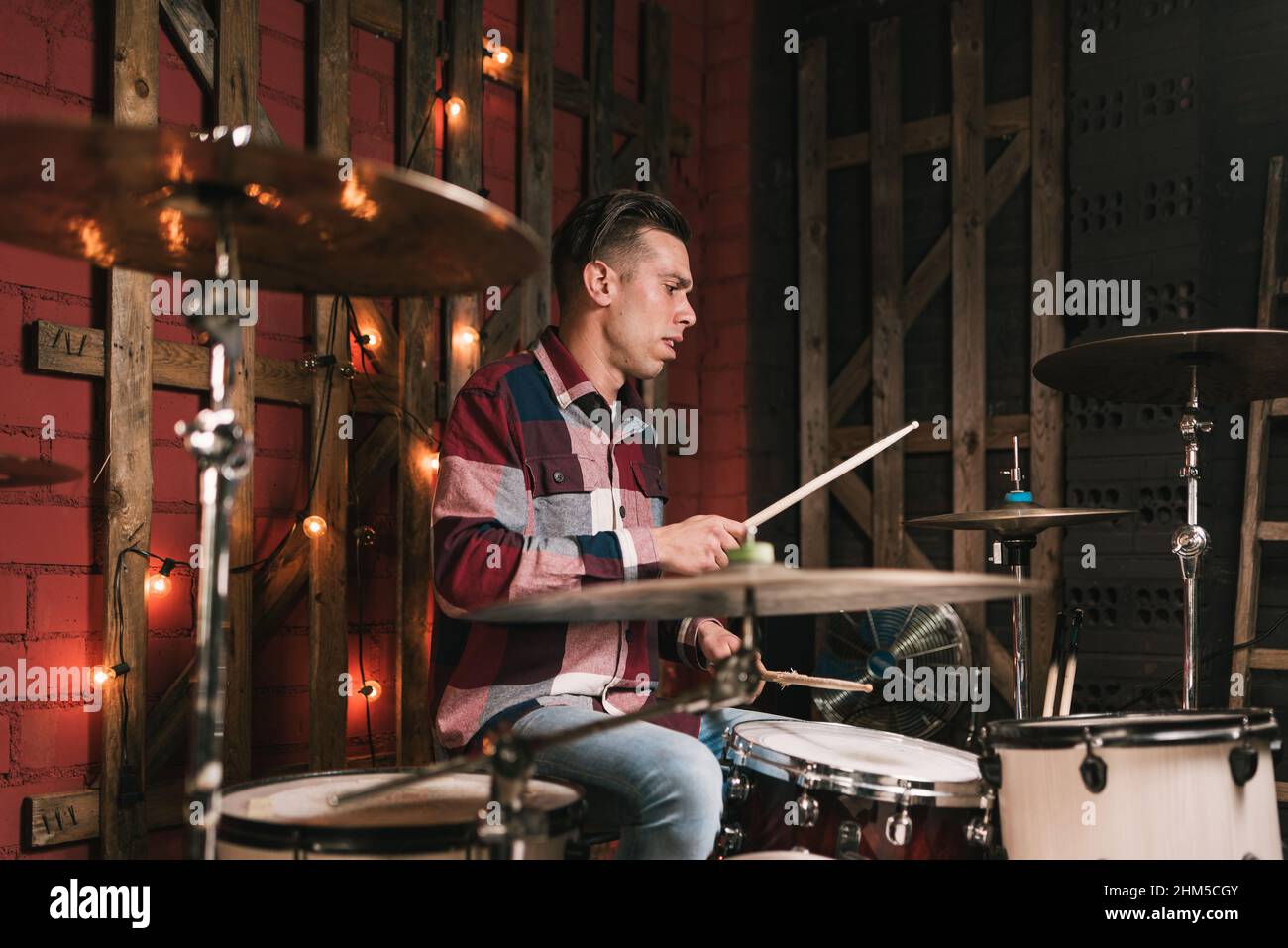 Uomo serio in casual vestire suonare la batteria e battere il ritmo in studio loft durante le prove musicali Foto Stock