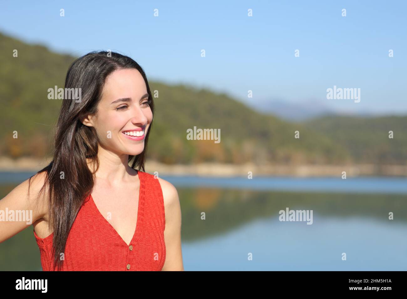 Donna felice in rosso guardando via in un lago in vacanza con spazio copia Foto Stock