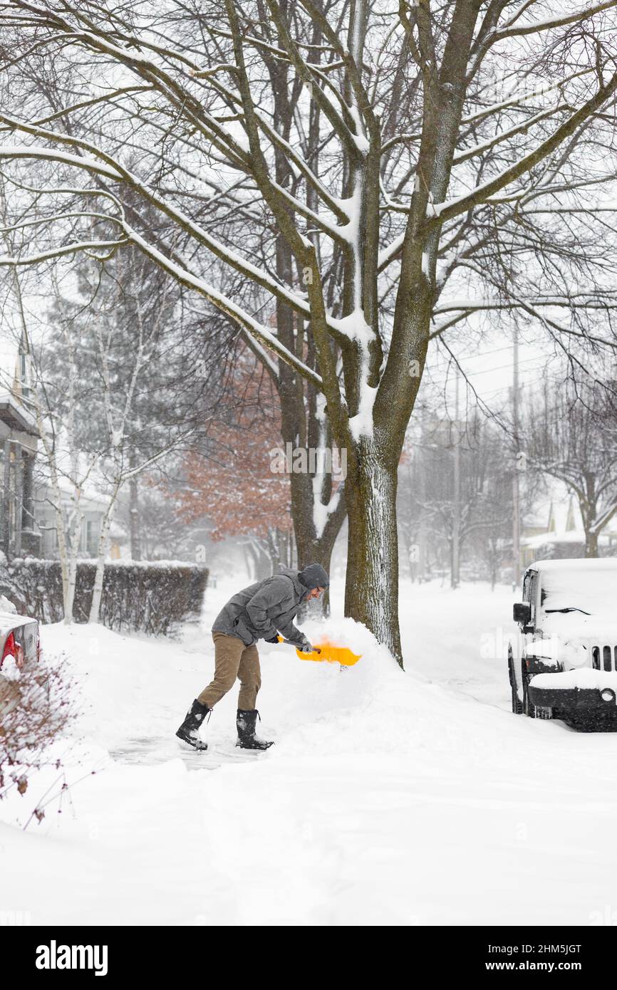 Uomo che pulisce un vialetto coperto di neve con una pala. Londra, Ontario. Canada Foto Stock