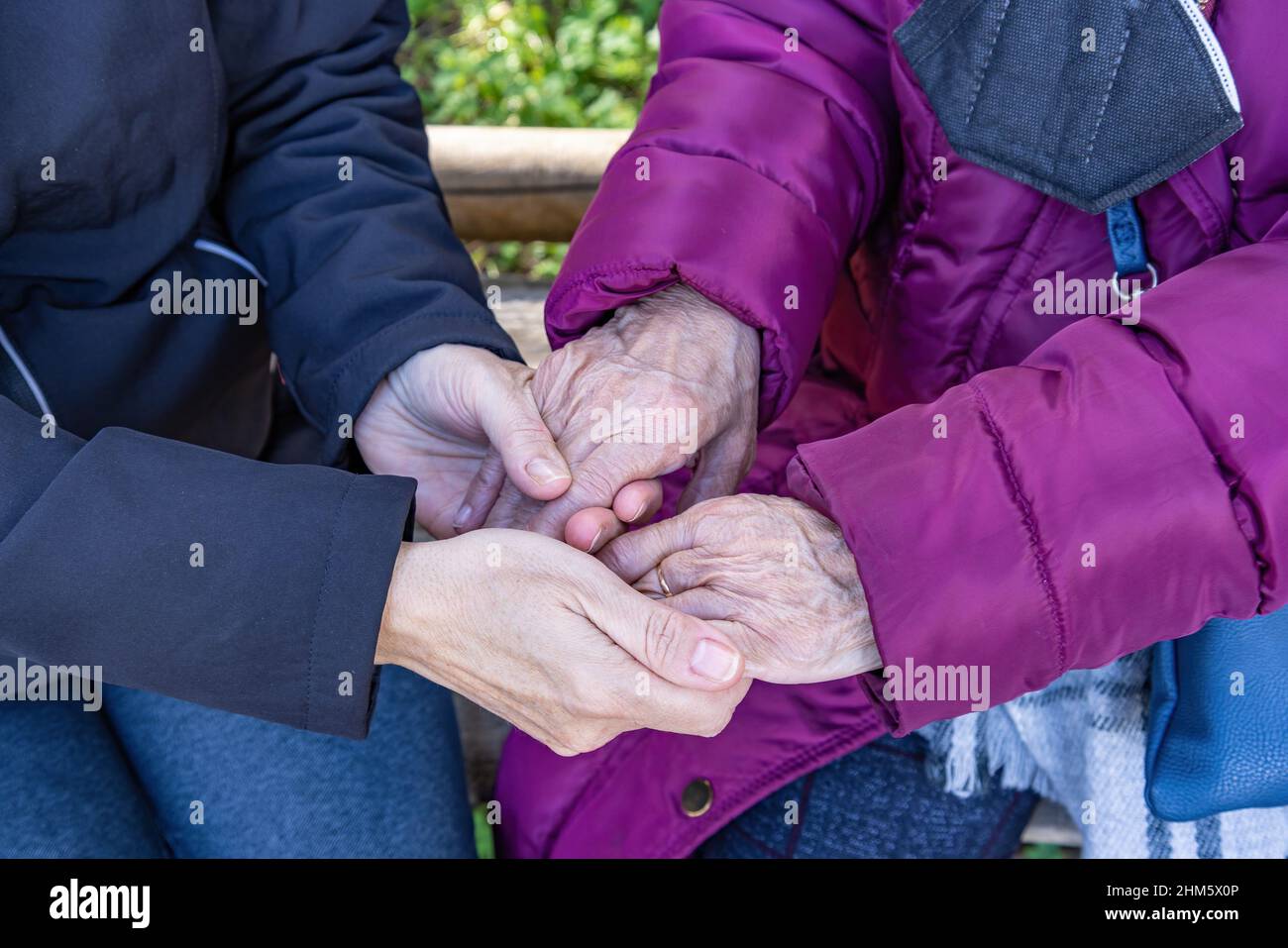 Una donna matura tiene le mani della madre anziana mentre si siedono su una panca Foto Stock