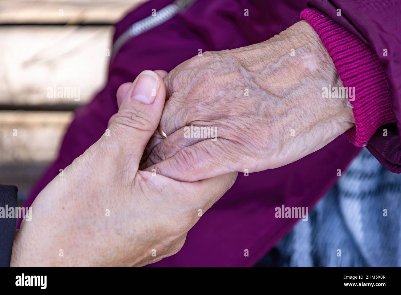 Una donna matura tiene la mano della madre anziana mentre siedono su una panca Foto Stock
