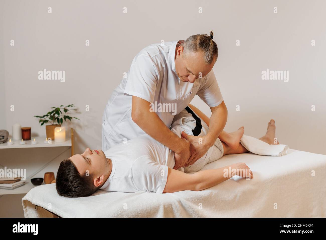 Massaggiatore forte e concentrato in uniforme che fa la terapia manuale per la schiena dell'atleta. Massaggio professionale e riabilitazione per sportivi. Concetto di benessere, corpo e assistenza sanitaria. Foto Stock