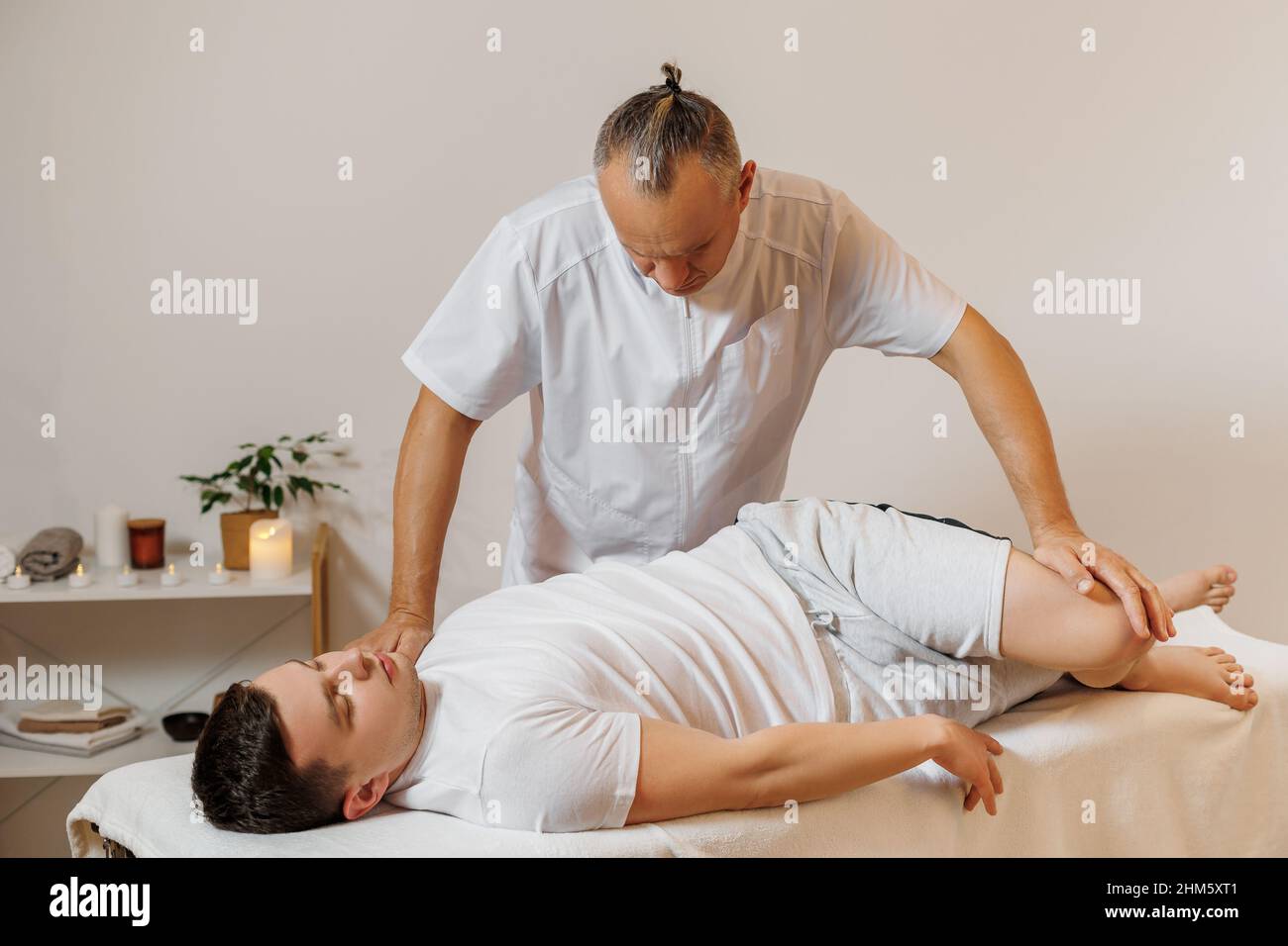 Massaggiatore forte e concentrato in uniforme che fa la terapia manuale per sportivo. Massaggio schiena professionale. Stretching muscolare posteriore. Concetto di benessere, corpo e assistenza sanitaria. Foto Stock