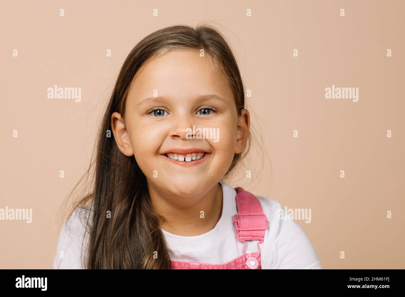 Ritratto del bambino con gli occhi luminosi e il sorriso felice eccitato con i denti superiori guardando la macchina fotografica che indossa il jumpsuit rosa brillante e la t-shirt bianca Foto Stock