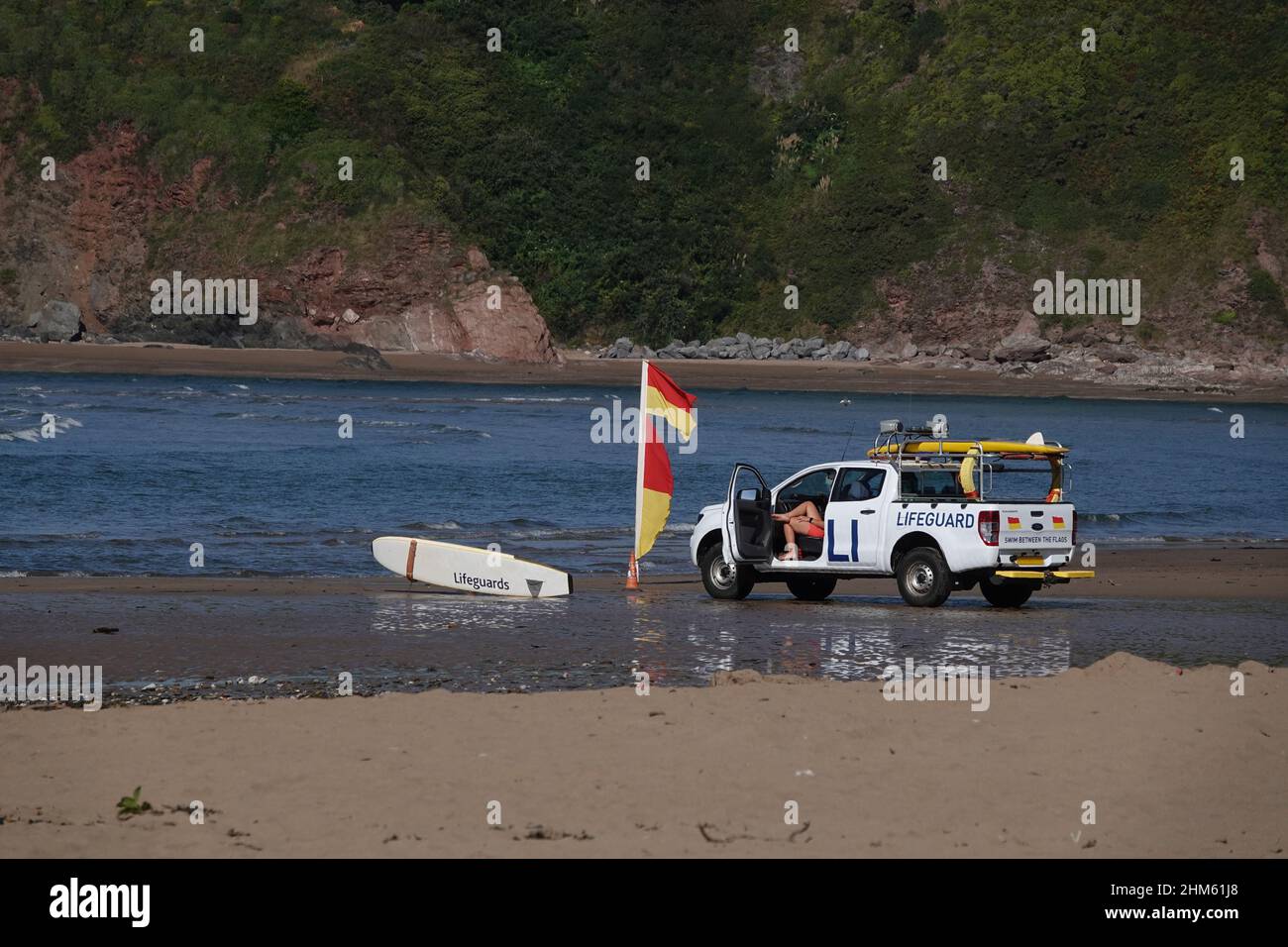 Bagnino seduto in un veicolo RNLI 4 x 4 su una spiaggia nel Regno Unito guardando i nuotatori, con bandiere di avvertimento battenti Foto Stock