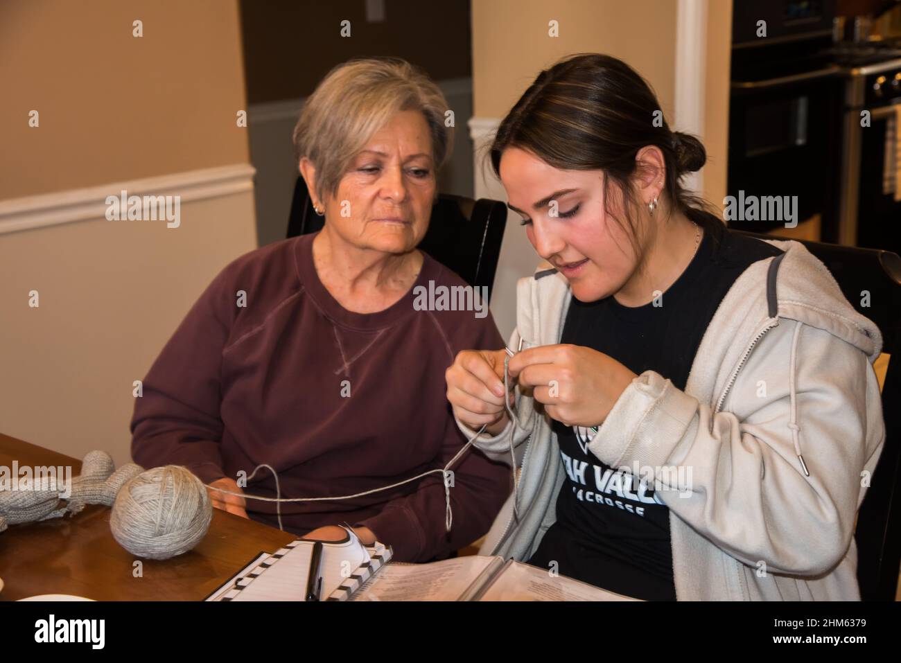 Nana guarda con un occhio critico come lei insegna a sua figlia grande come lavorare a maglia. L'arte e l'arte della maglieria si perdono nella generazione millenaria. Foto Stock