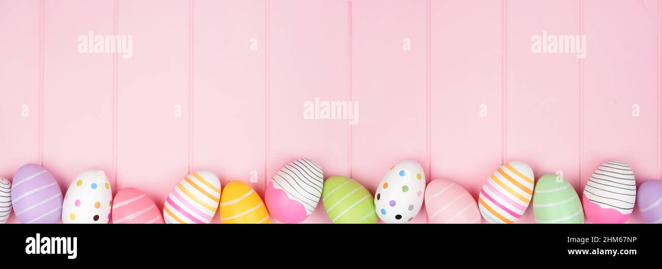 Colorato bordo inferiore dell'uovo di Pasqua su un morbido sfondo di legno rosa banner. Vista dall'alto verso il basso con spazio di copia. Foto Stock