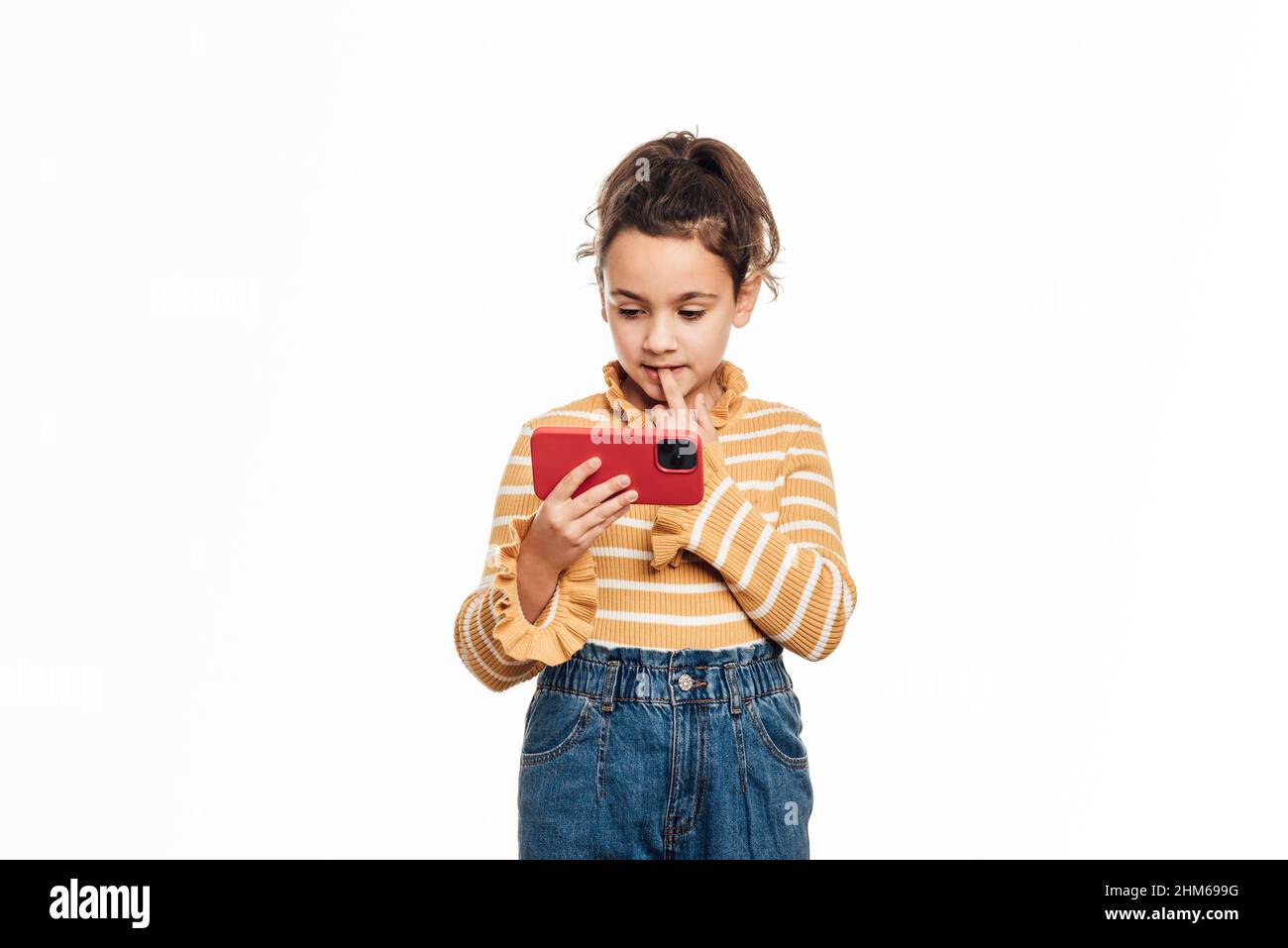 Ragazza che guarda qualcosa sul suo cellulare mentre si alza su uno sfondo bianco isolato. Foto Stock