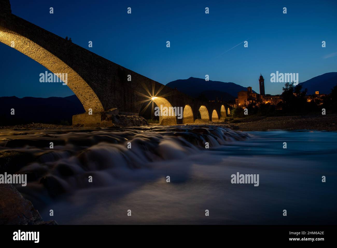 Il Ponte Gobbo è un antico ponte romano dal profilo irregolare al tramonto che attraversa il fiume Trebbia a Bobbio Foto Stock