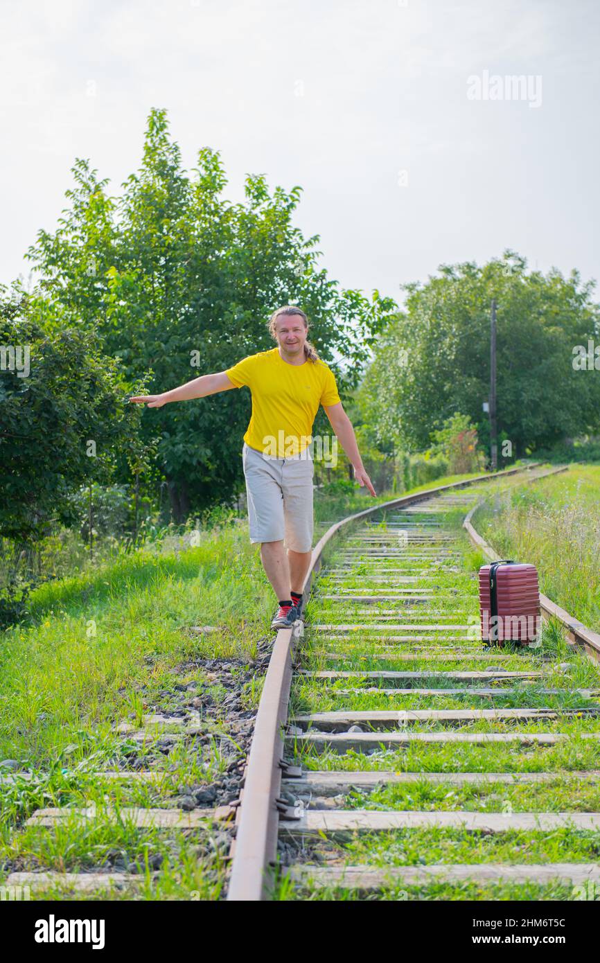 il viaggiatore freddo con una valigia rossa sulle rotaie va Foto Stock