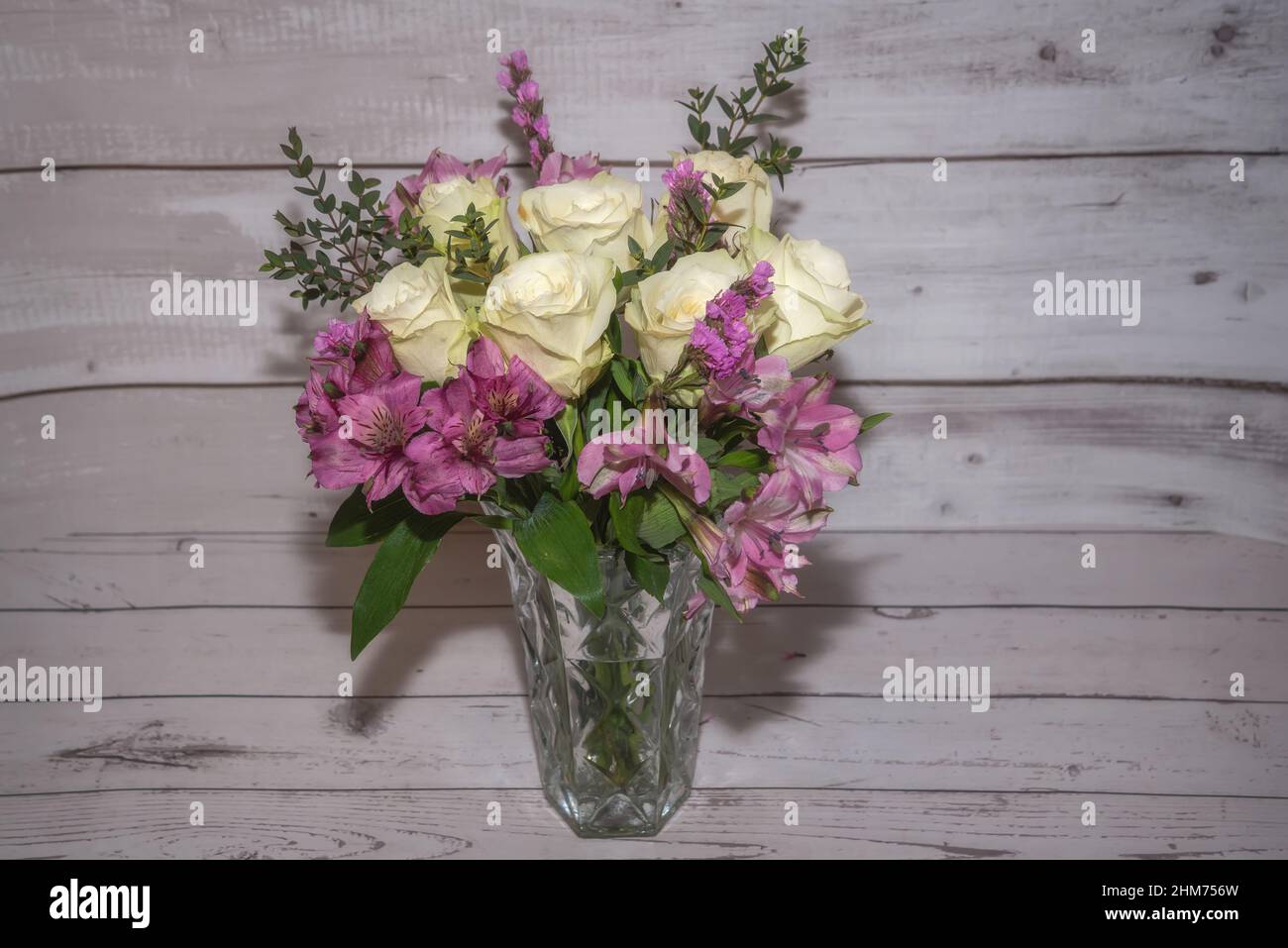 Bel bouquet delicato con rose bianche e alstroemeria in vaso sullo sfondo di un vecchio muro di legno bianco Foto Stock